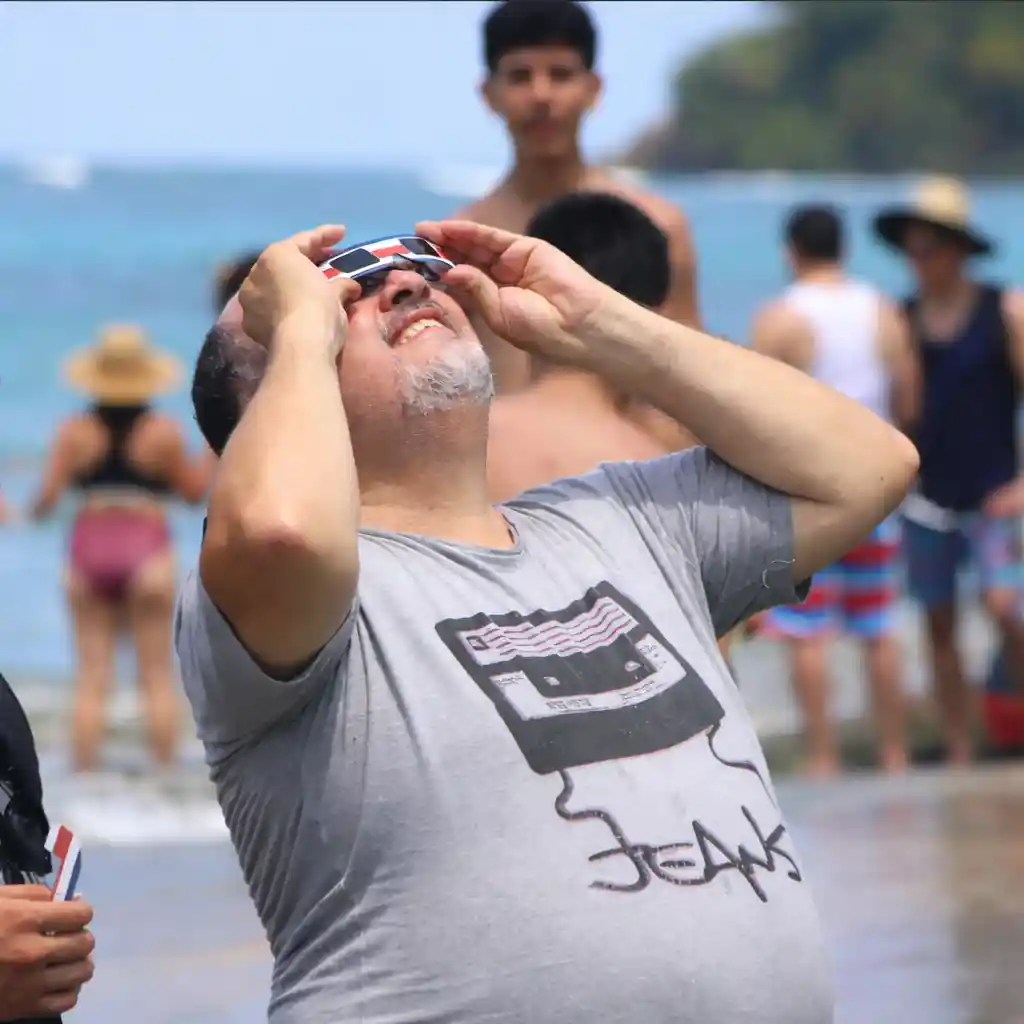 Persona usando gafas de eclipse solar con temática de Costa Rica en la playa.